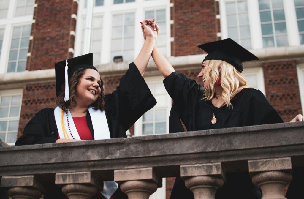 Two female college graduates celebrating success outside a university building.